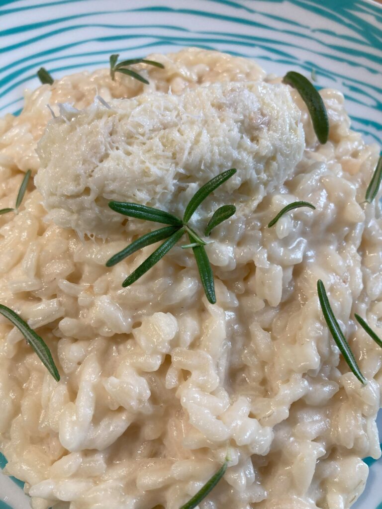 Risotto al latte di baccalà visto da vicino e decorato con rosmarino e quebelle di baccalà mantecato